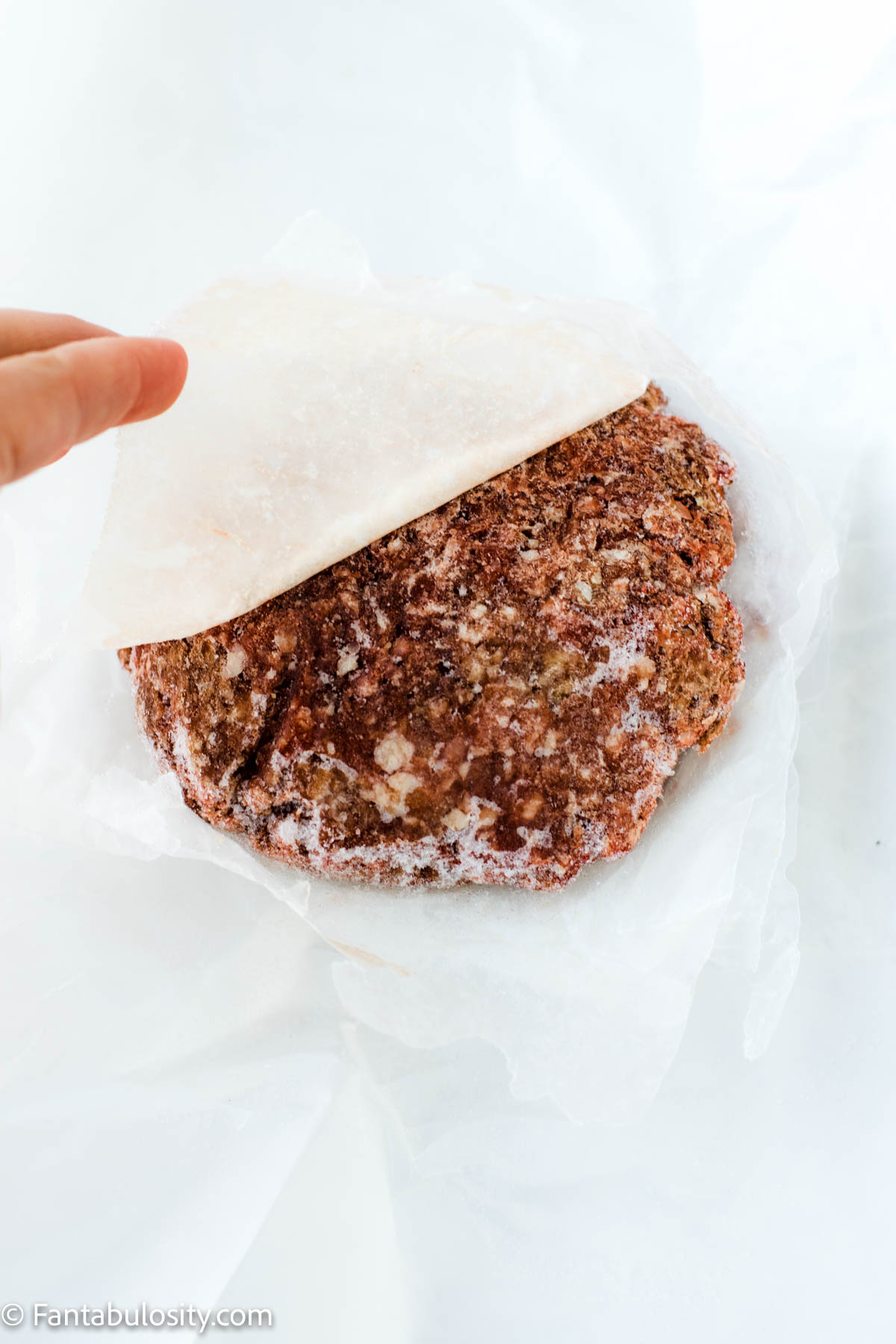 Hamburger patties placed between pieces of wax paper.