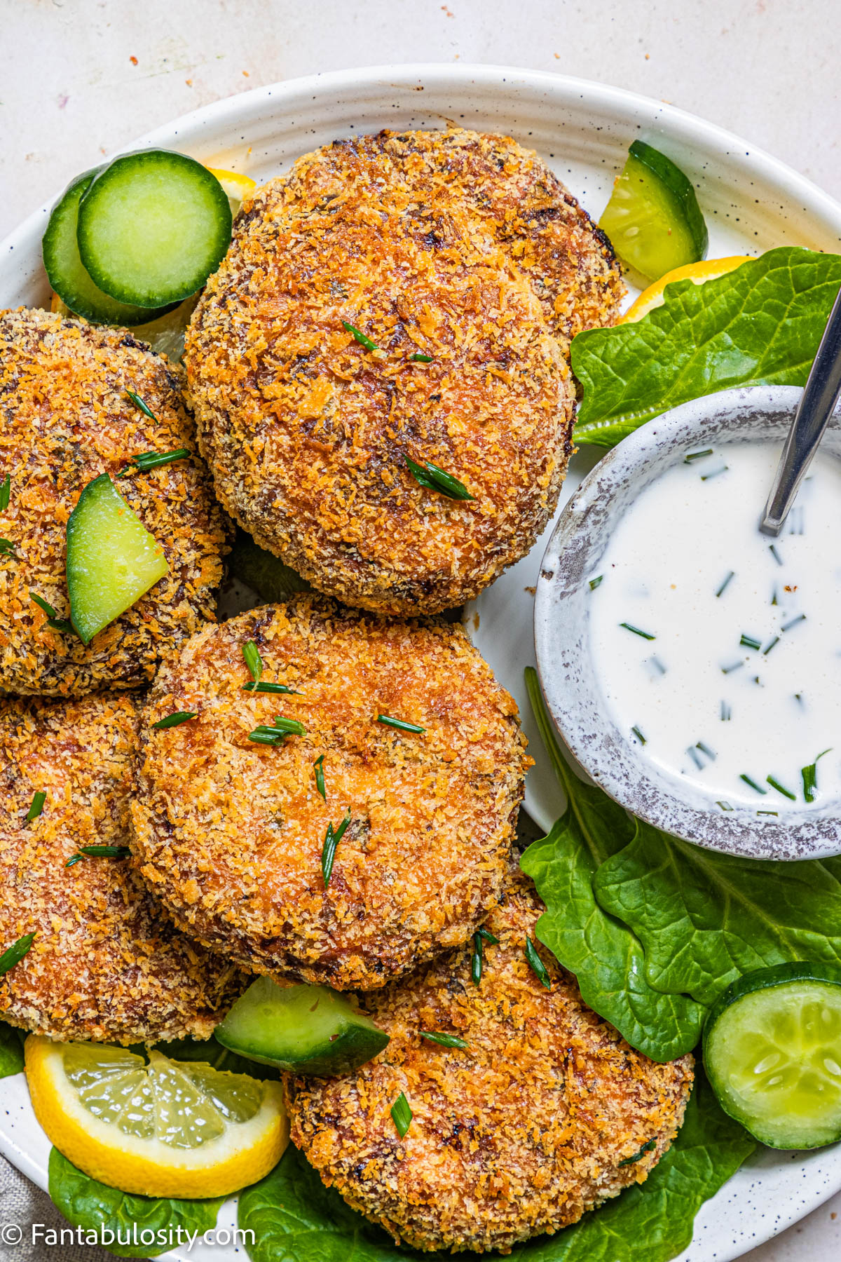 
Salmon patties with cucumbers and lemons on a plate.
