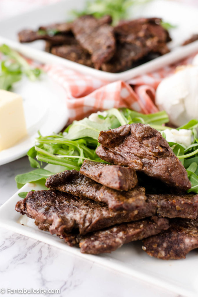 Air Fryer Venison Steak on a white plate surrounded by salad and butter