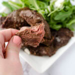 Air fryer deer meat on platter and hand holding a piece.