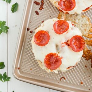 Bagel pizza topped with pepperonis on baking sheet.