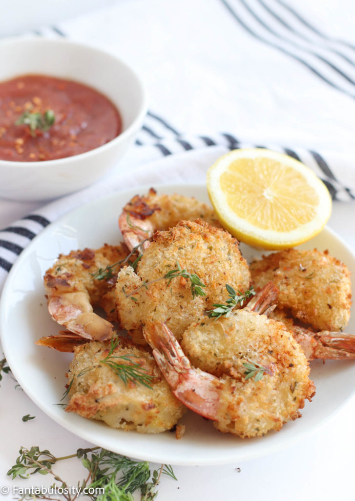 
A plate of fried shrimp with cocktail sauce and a lemon wedge.
