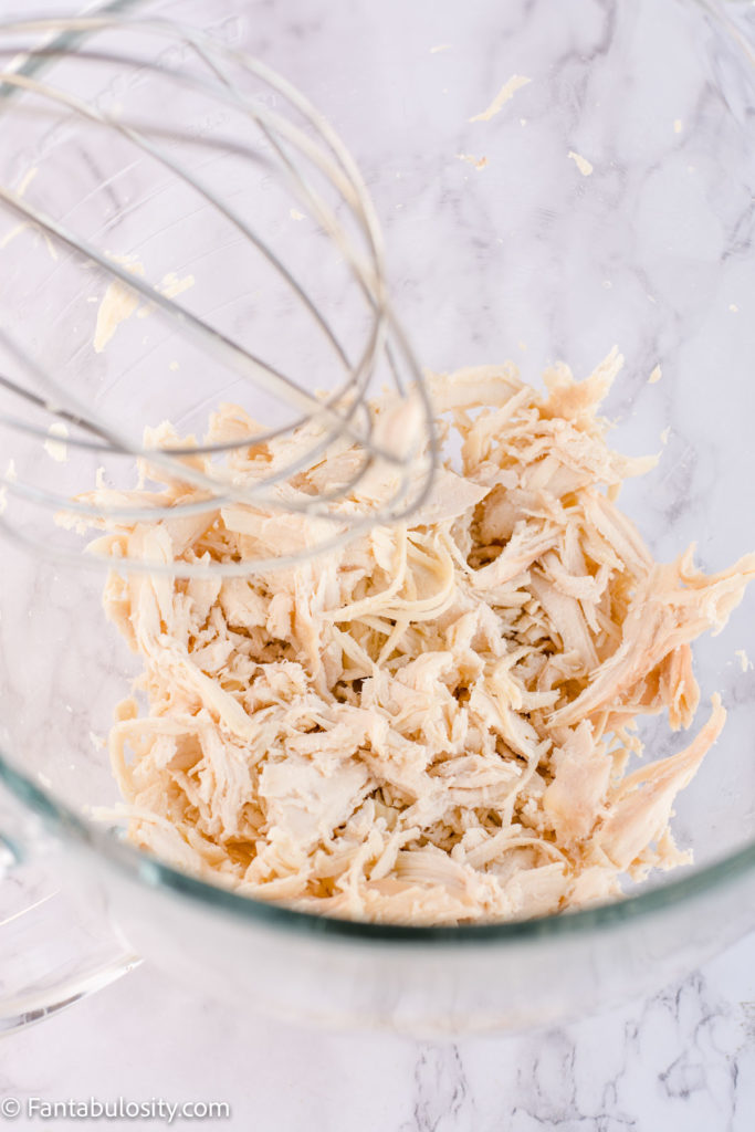 shredded rotisserie chicken in a mixing bowl with a whisk