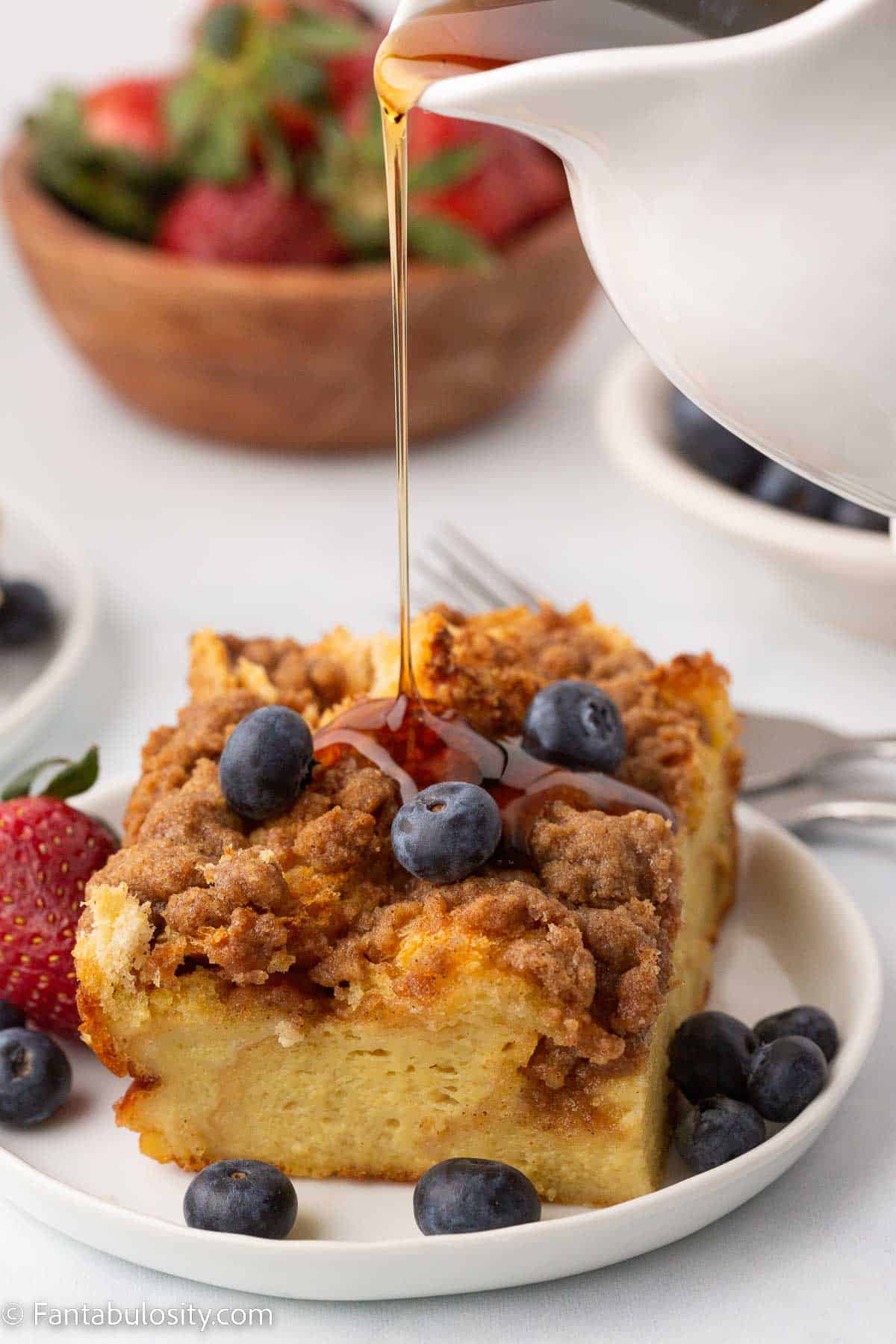 Syrup pouring over French toast casserole in white plate with blueberries.