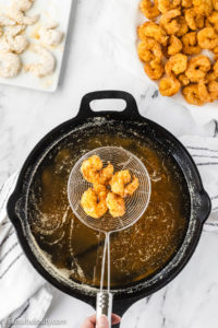 Shrimp in mesh ladle, being pulled out of cast iron pan