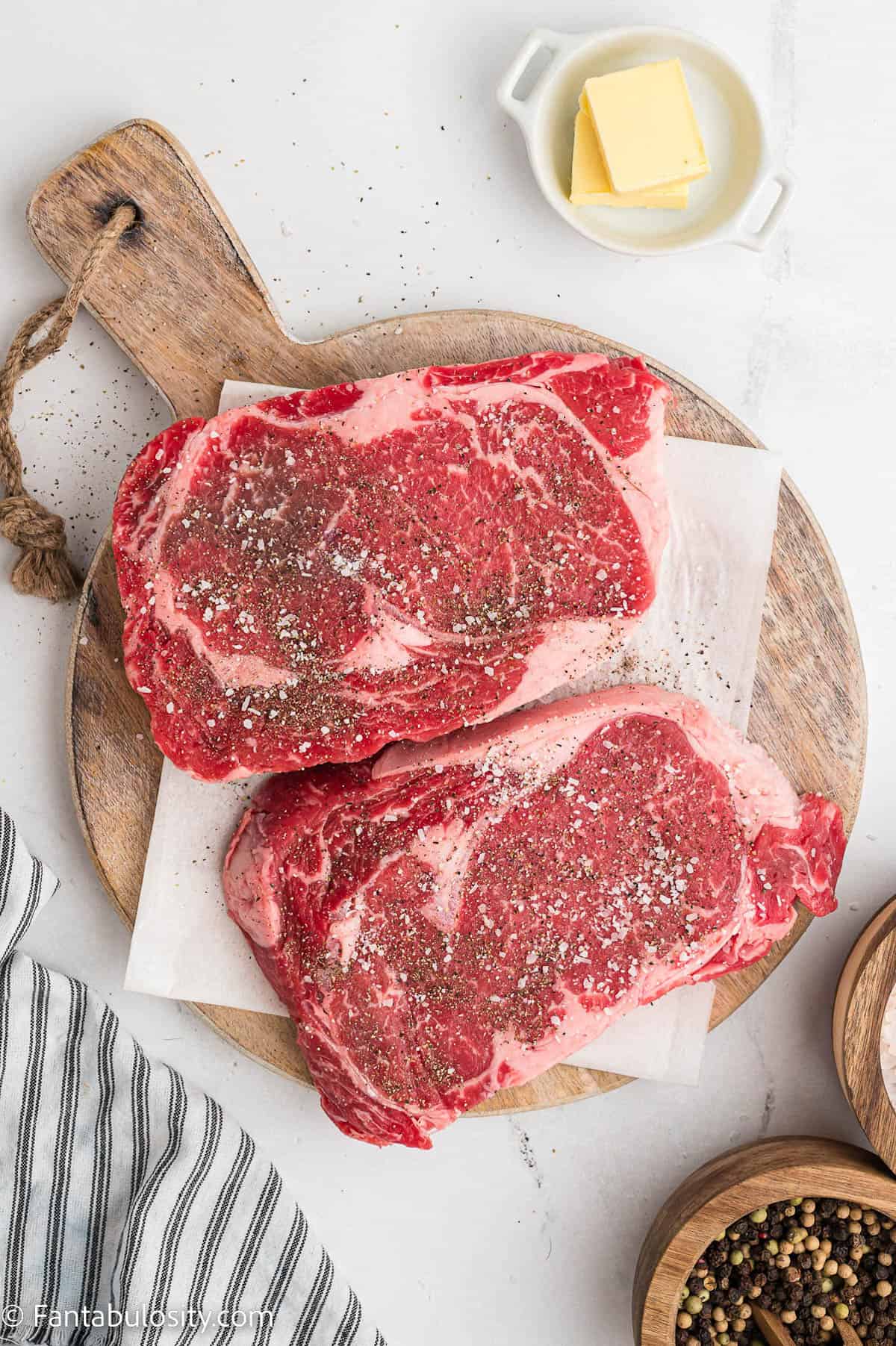 T-bone steak fillets on cutting board with salt and pepper sprinkled on them