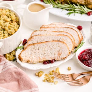 sliced Instant Pot turkey breast on a white plate with side dishes surrounding