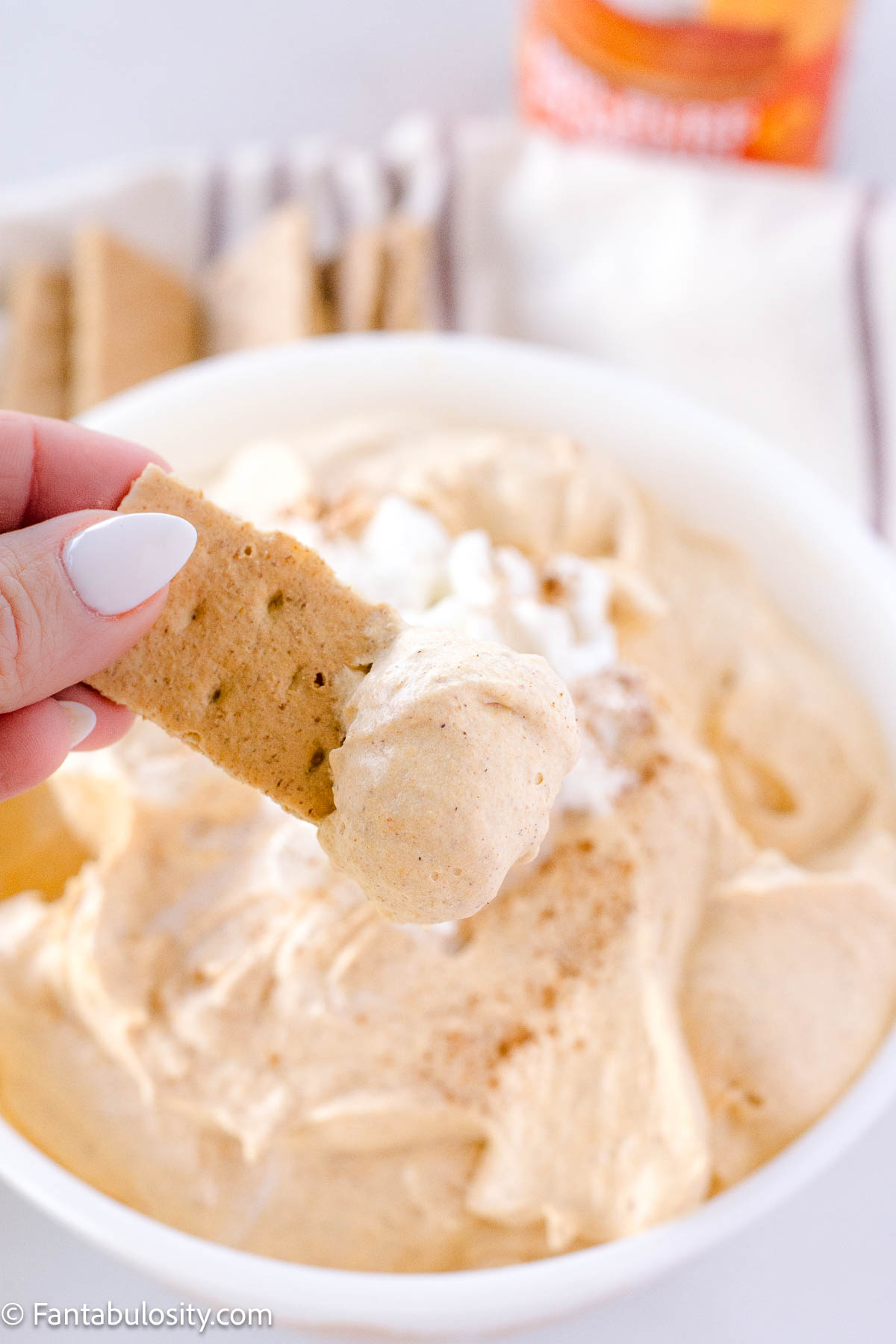 Hand holding graham cracker that has been dipped in to pumpkin fluff.