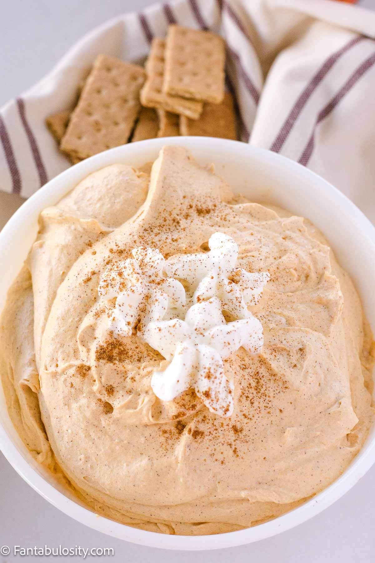 Pumpkin Pie Fluff in serving bowl, topped with Reddi Wip and pumpkin pie spice, sitting next to graham crackers.