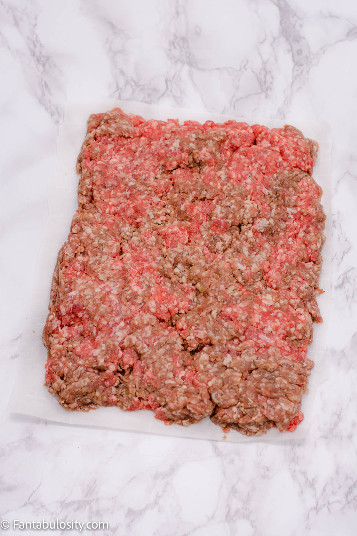 raw ground beef shaped on parchment paper