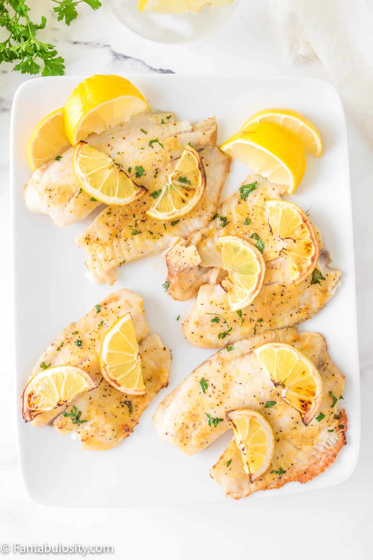 
A platter of air fryer tilapia with lemon wedges.
