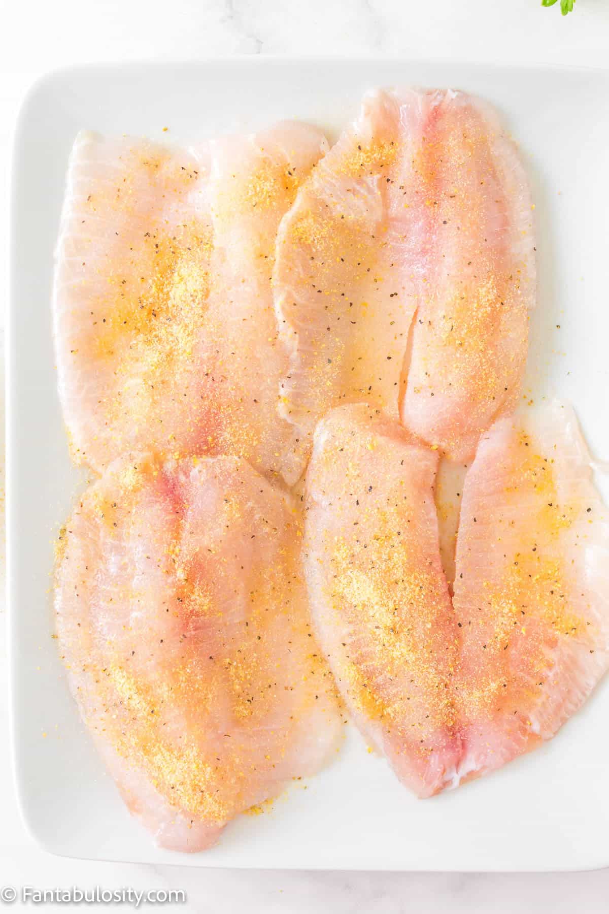 Raw fillets of tilapia with spices on them.