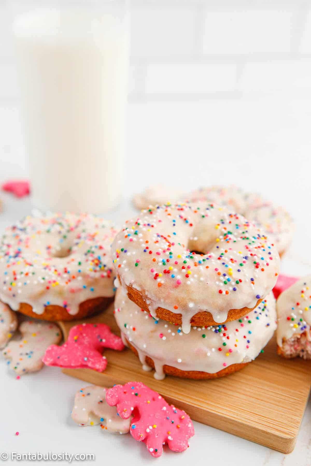 Stacked circus animal Cookie Donuts, next to a glass of milk
