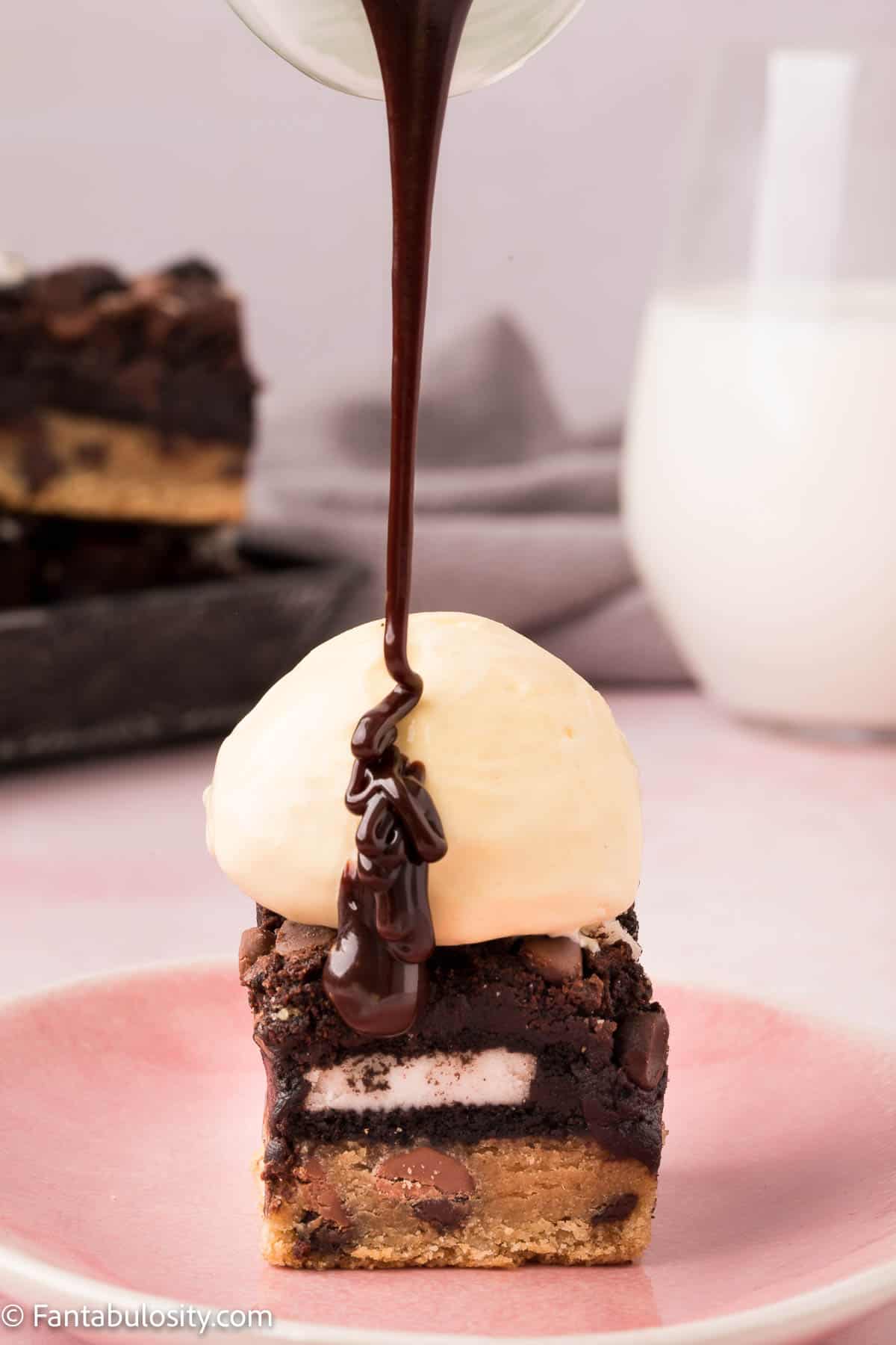 Drizzling chocolate sauce on top of ice cream covered Oreo Brookies.