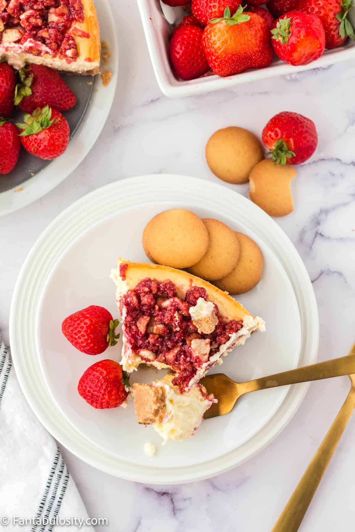 A slice of strawberry crunch cheesecake on plate with vanilla wafers and strawberries