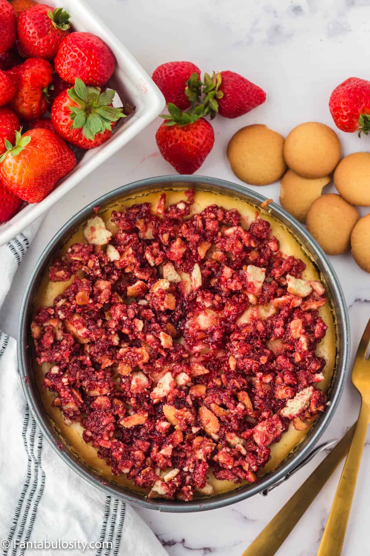 Cheesecake topped with strawberry crunch topping, still in cheesecake pan.