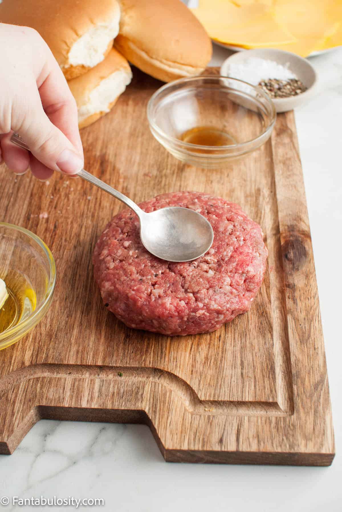 A spoon making a diet in the top of the burger patty.