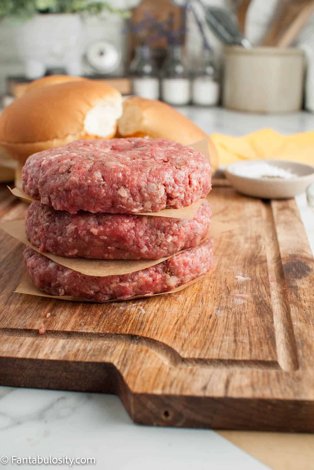 A stack of three Juicy Lucy burger patties with wax paper between them.