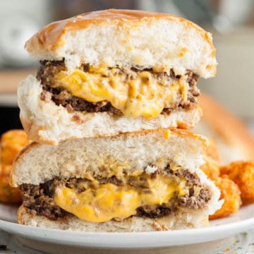 A juicy Lucy burger cut in half so we can see the cheese inside and stacked one half on top of the other.
