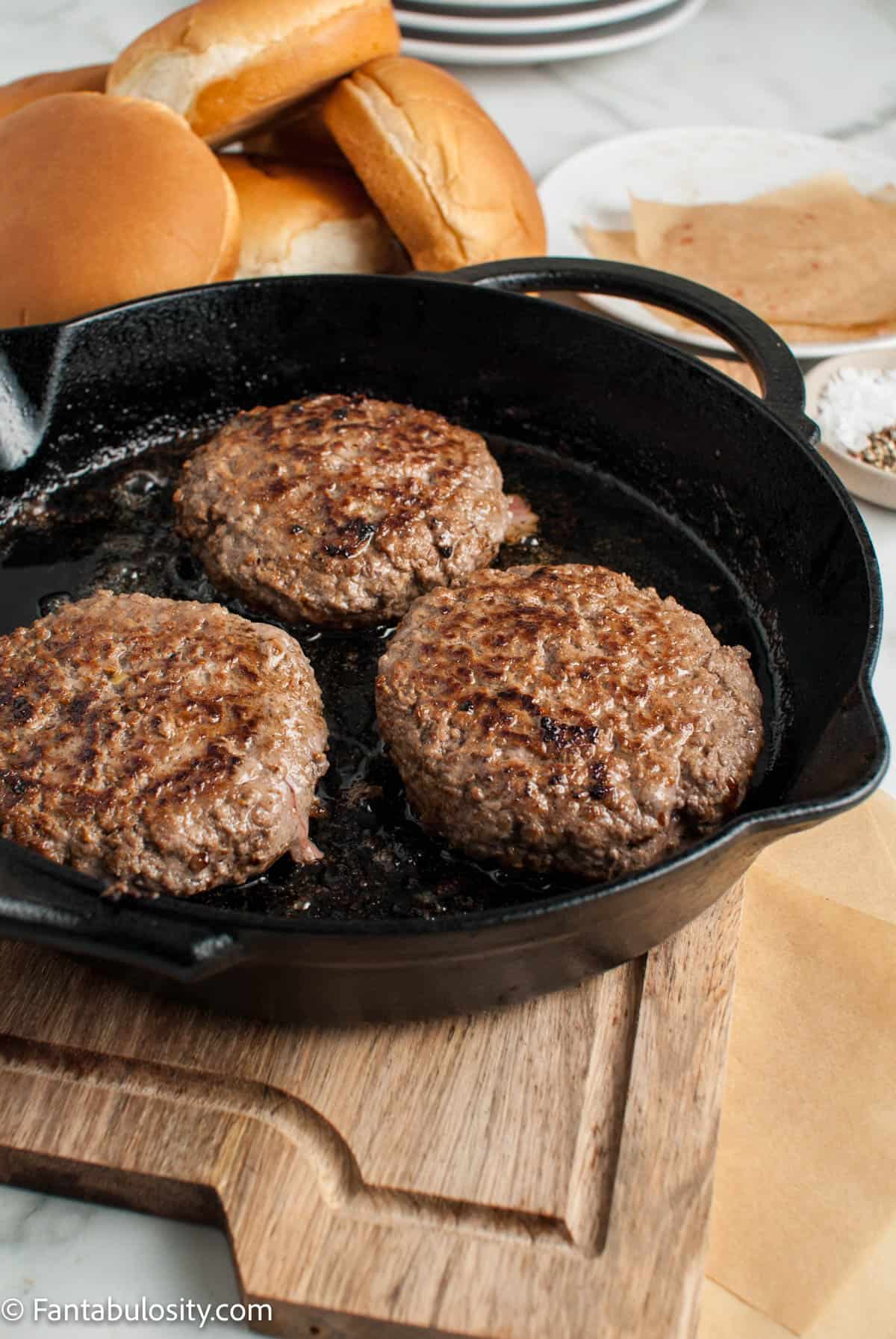 Three cooked burger patties in a large skillet.