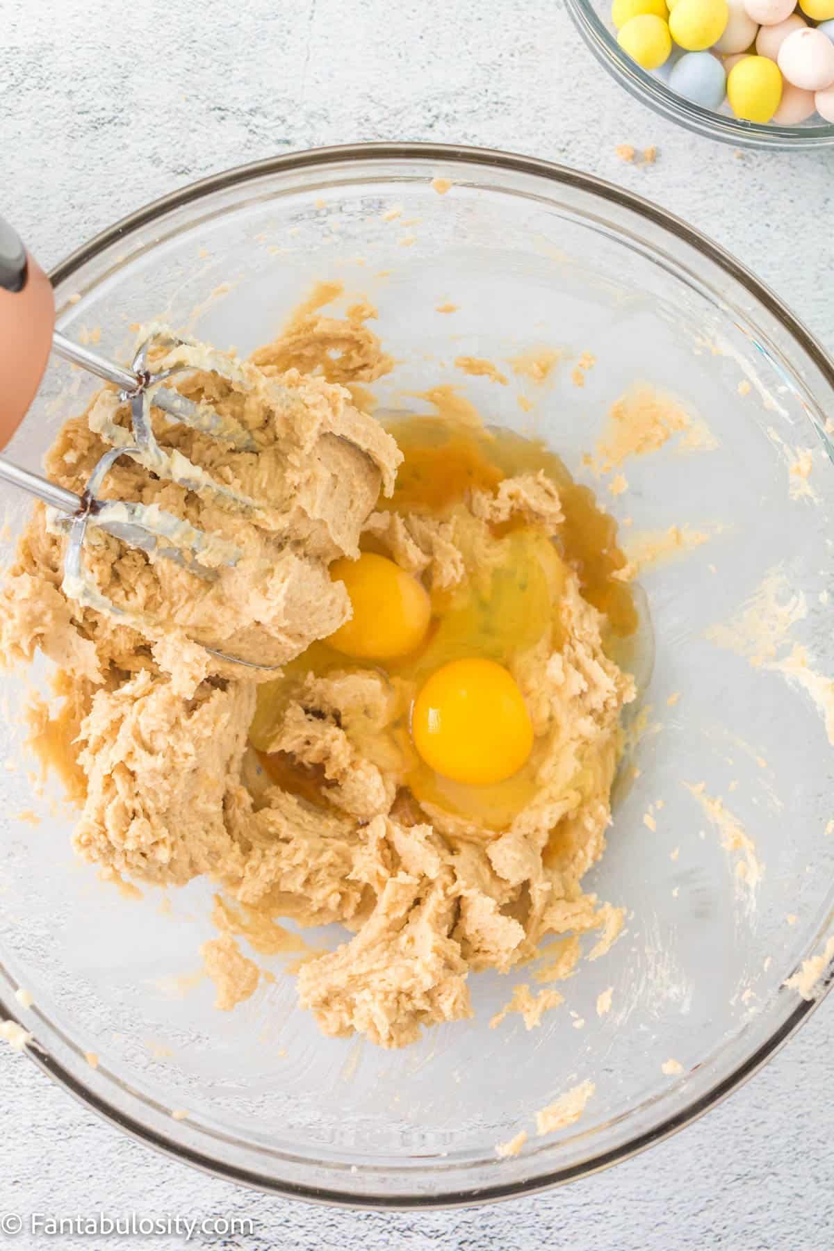 Eggs being mixed into the creamed butter mixture with an electric handheld mixer.