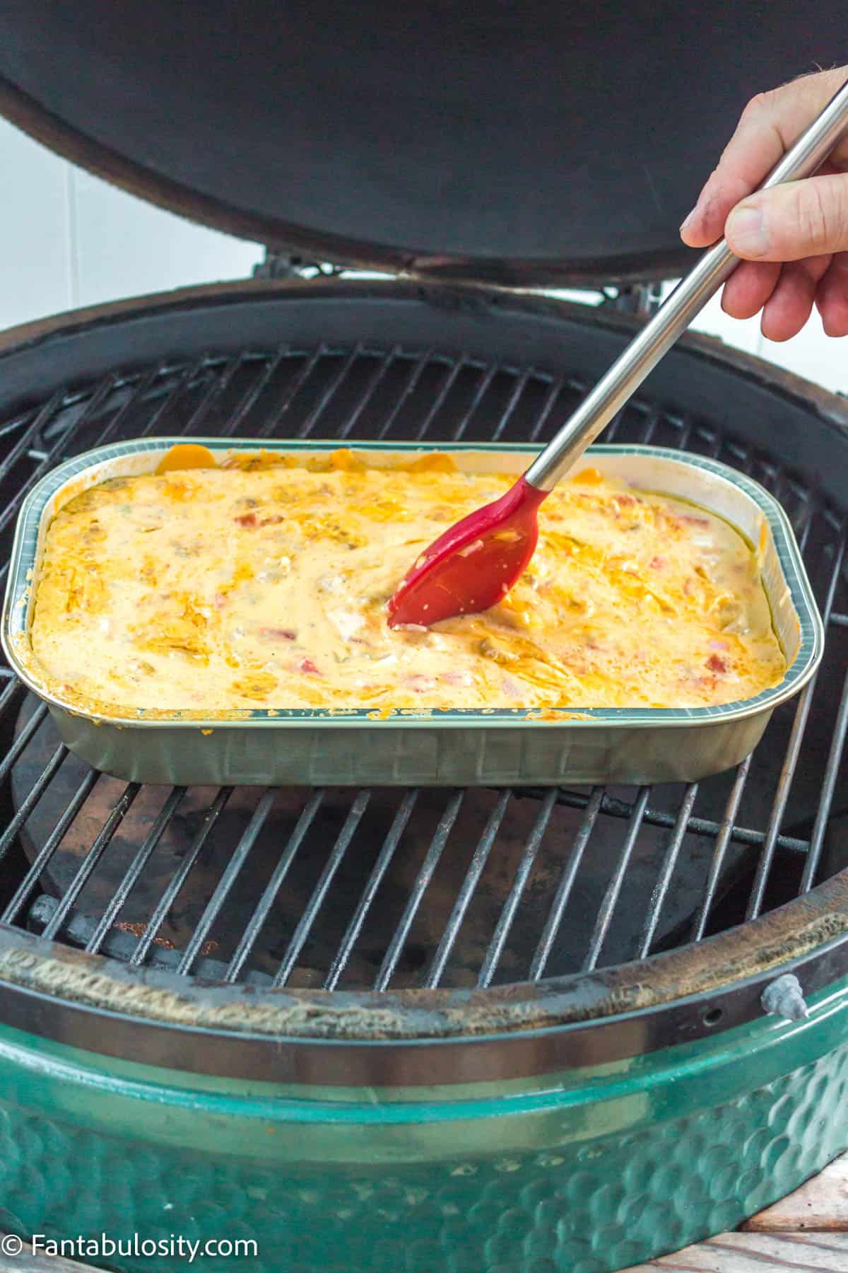 A spatula stirring the queso while it cooks on the charcoal grill.