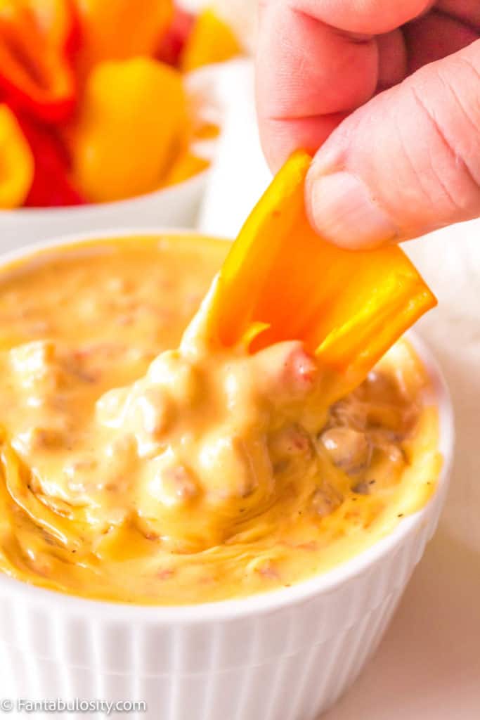 A close up of someone dipping a bell pepper into the smoked quest dip.