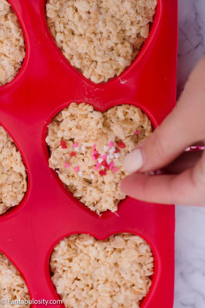 hand pouring sprinkles on heart-shaped rice crispy treats