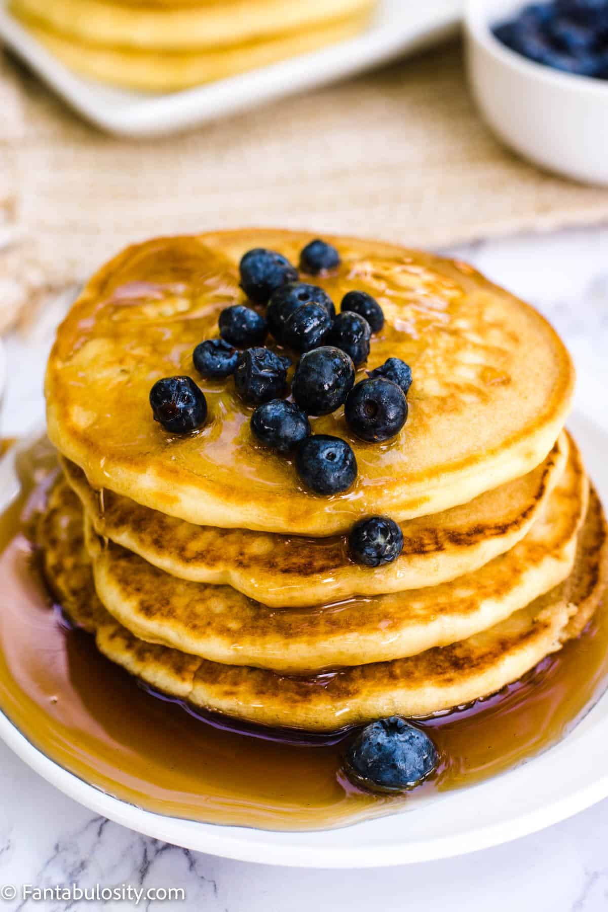 Almond milk pancakes stacked with syrup on and around them and blueberries on top of the stack. 