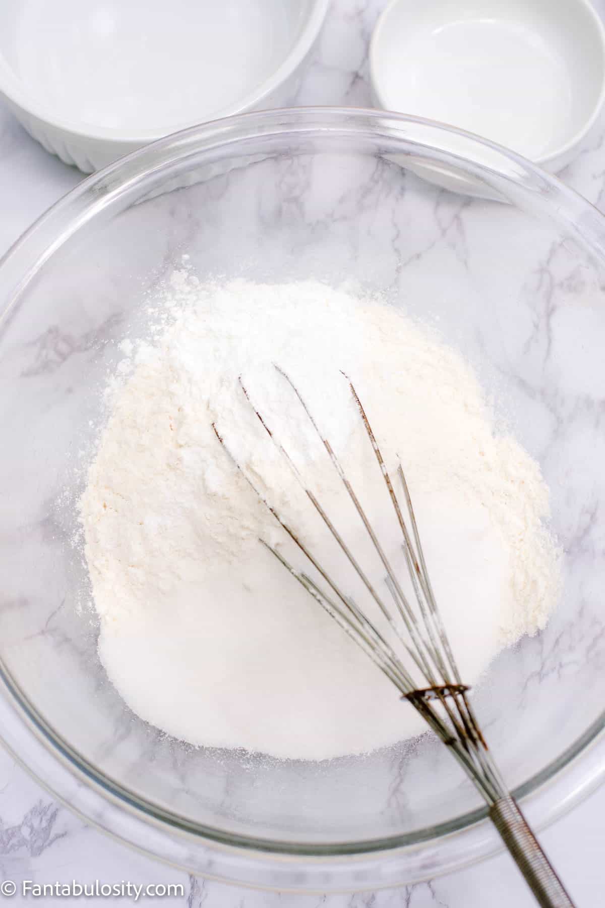 A whisk mixing up dry ingredients in a glass bowl.