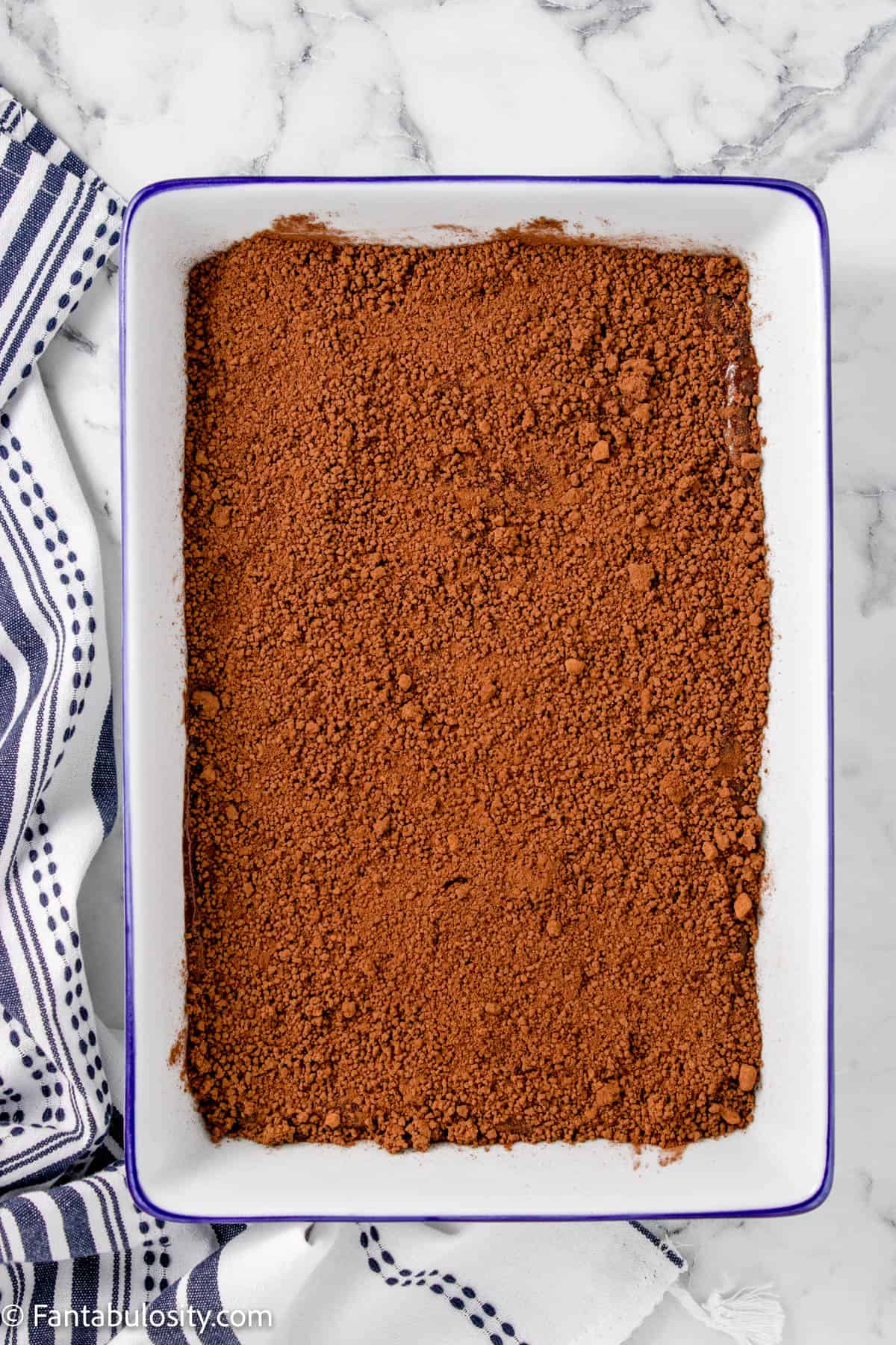 Brown sugar and cocoa mixture spread out over cake batter in the rectangle baking dish.