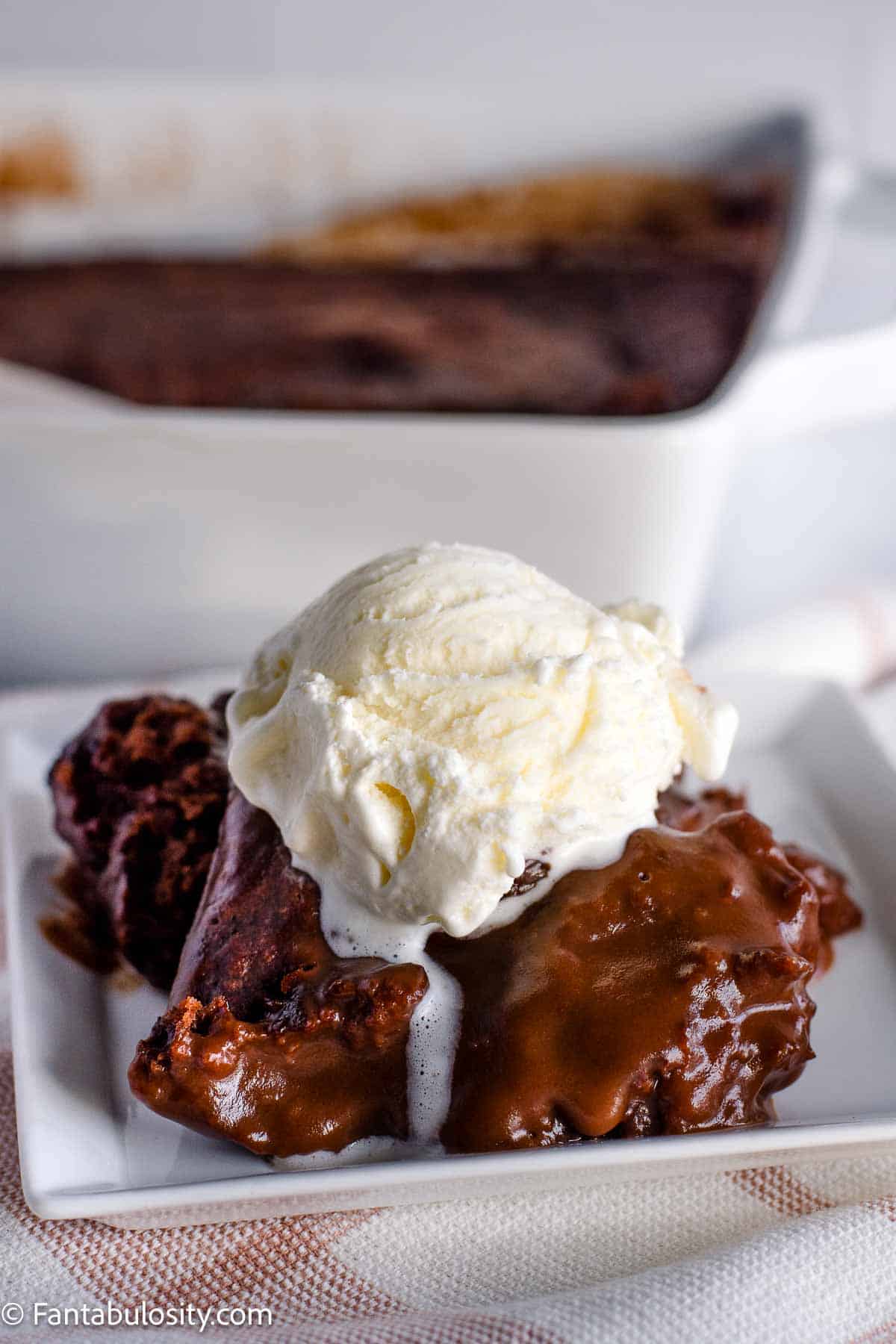 Hot fudge cake sitting on white, square plate with a scoop of vanilla ice cream on top.