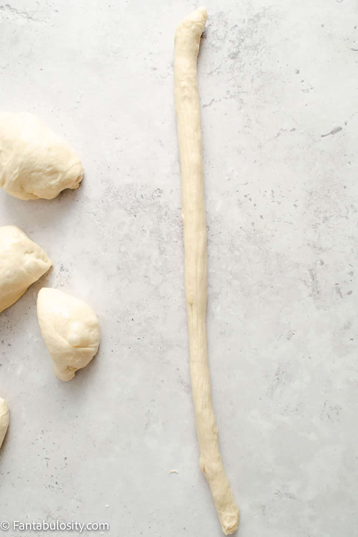 One ball of pretzel dough rolled out into a long rope-like line.