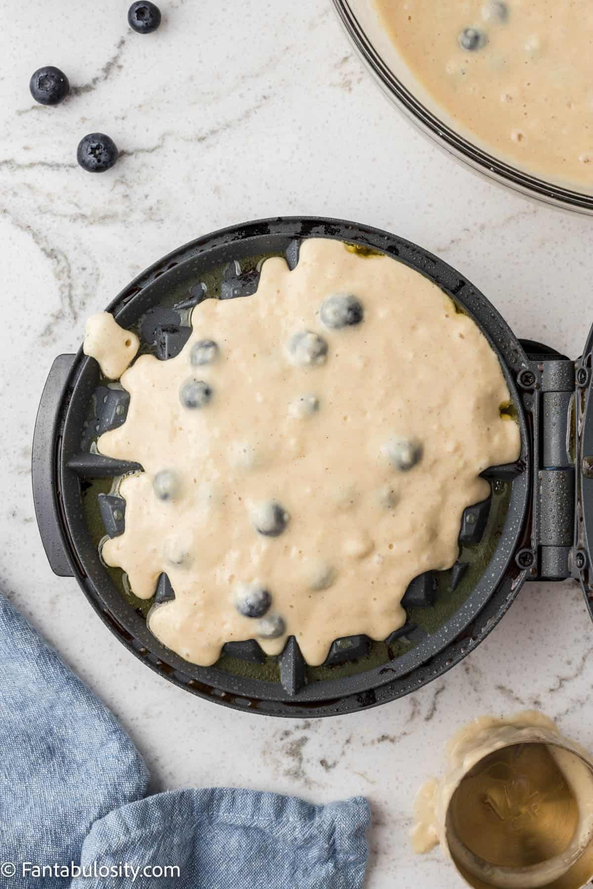 Blueberry waffle batter on a waffle maker bottom iron.