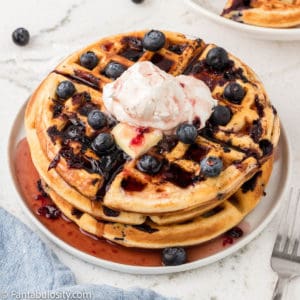 Blueberry waffles on a plate, drenched in syrup.