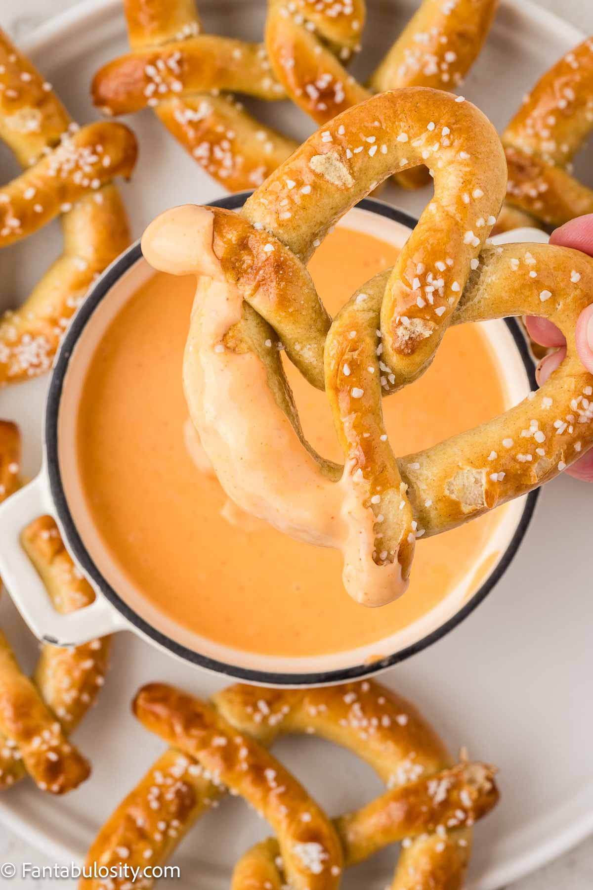 Soft pretzel being dipped in to cheese sauce.