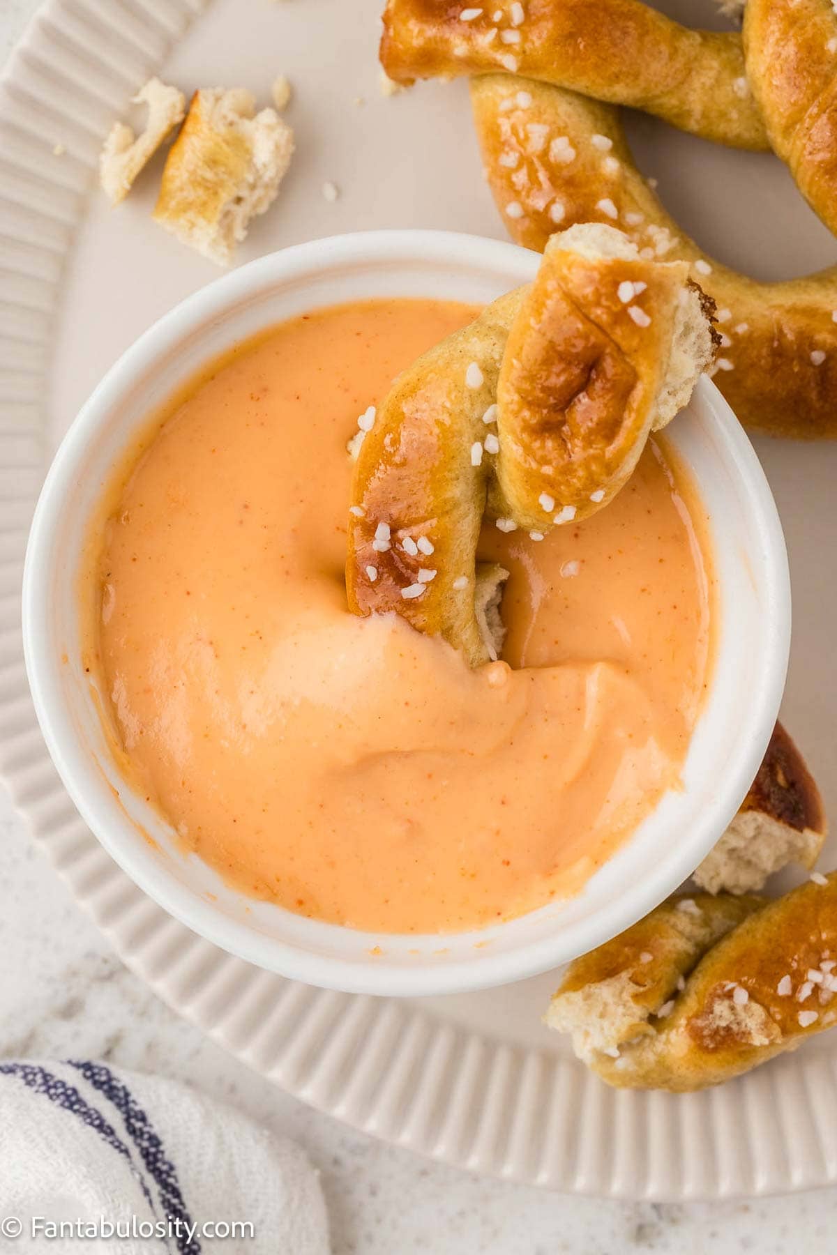 Cheese sauce in round bowl, with soft pretzel dipped in.