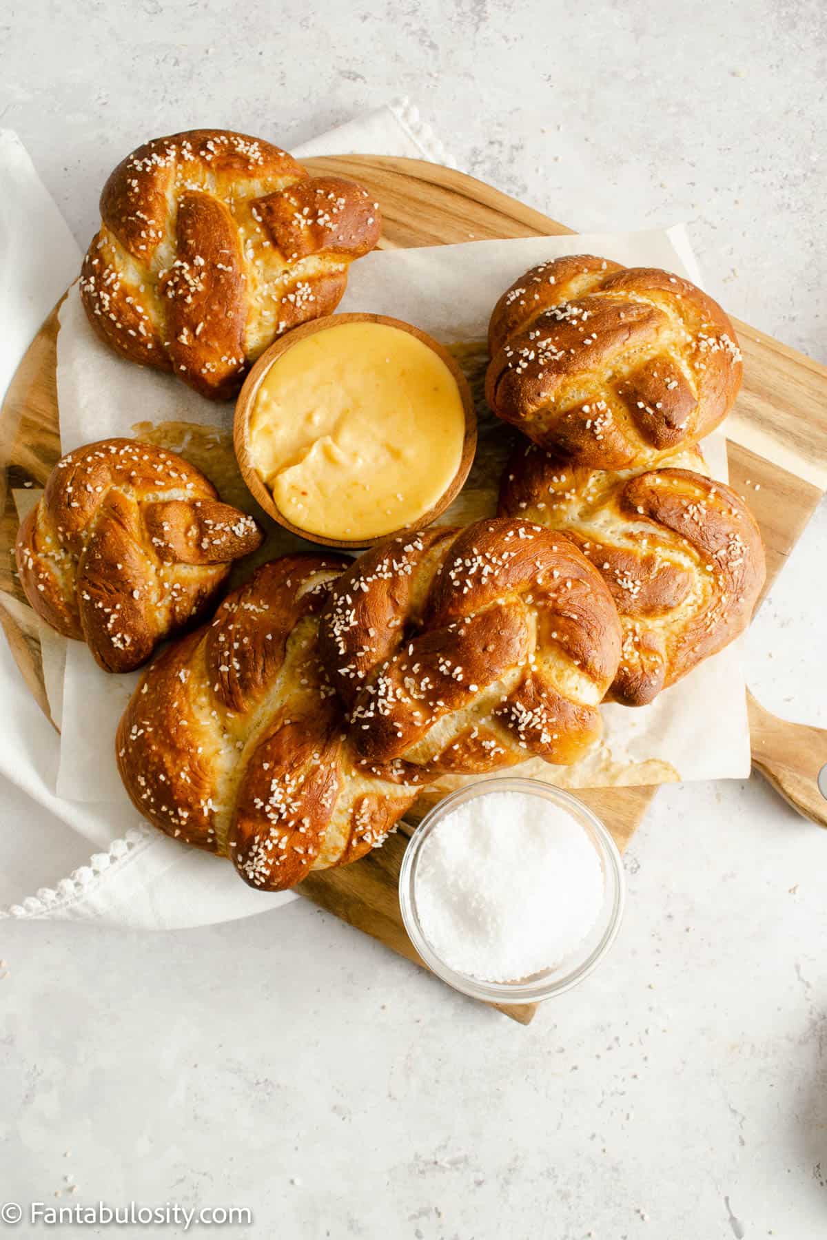 Pretzel cheese dip surrounded by soft pretzels on a wood tray.