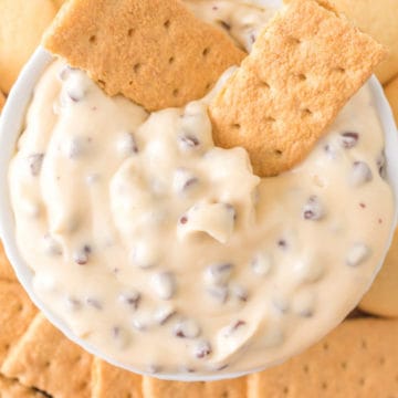 A bowl of booty dip surrounded by crackers and with two graham crackers in the dip.