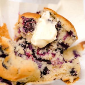 A buttermilk blueberry muffin cut in half with butter on one half.