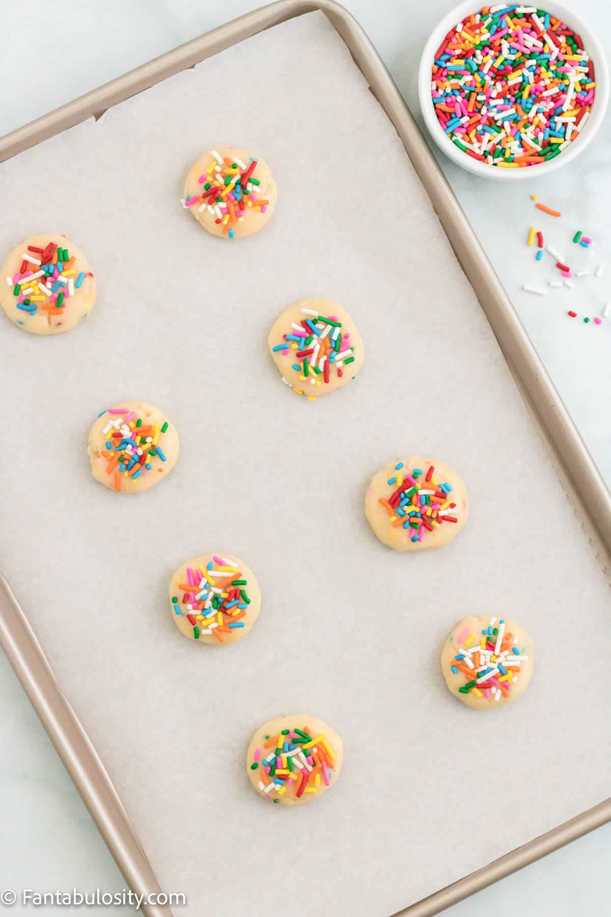 Uncooked balls of funfetti cake mix cookies on a parchment lined baking sheet.