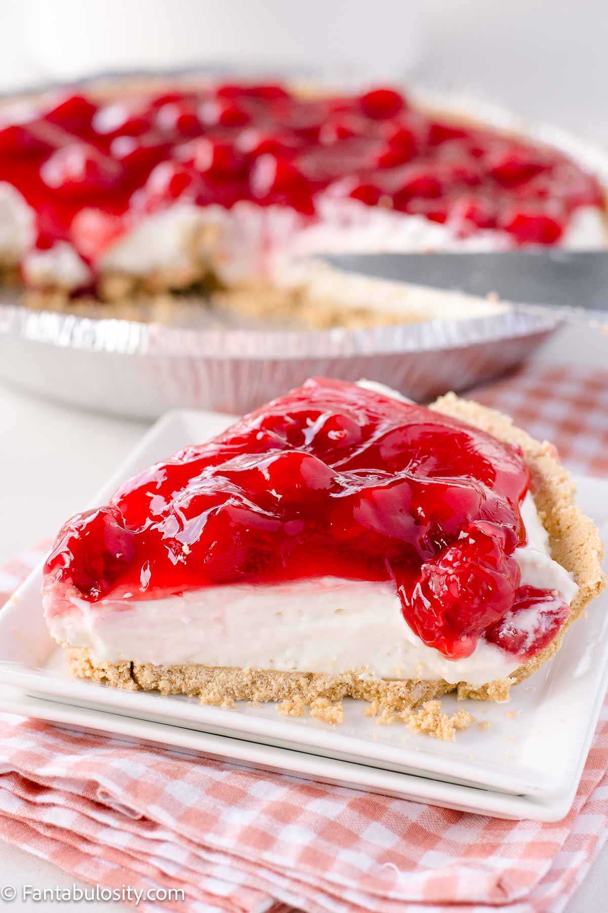 Slice of no bake cherry cheesecake on a plate, next to the rest of the pie.