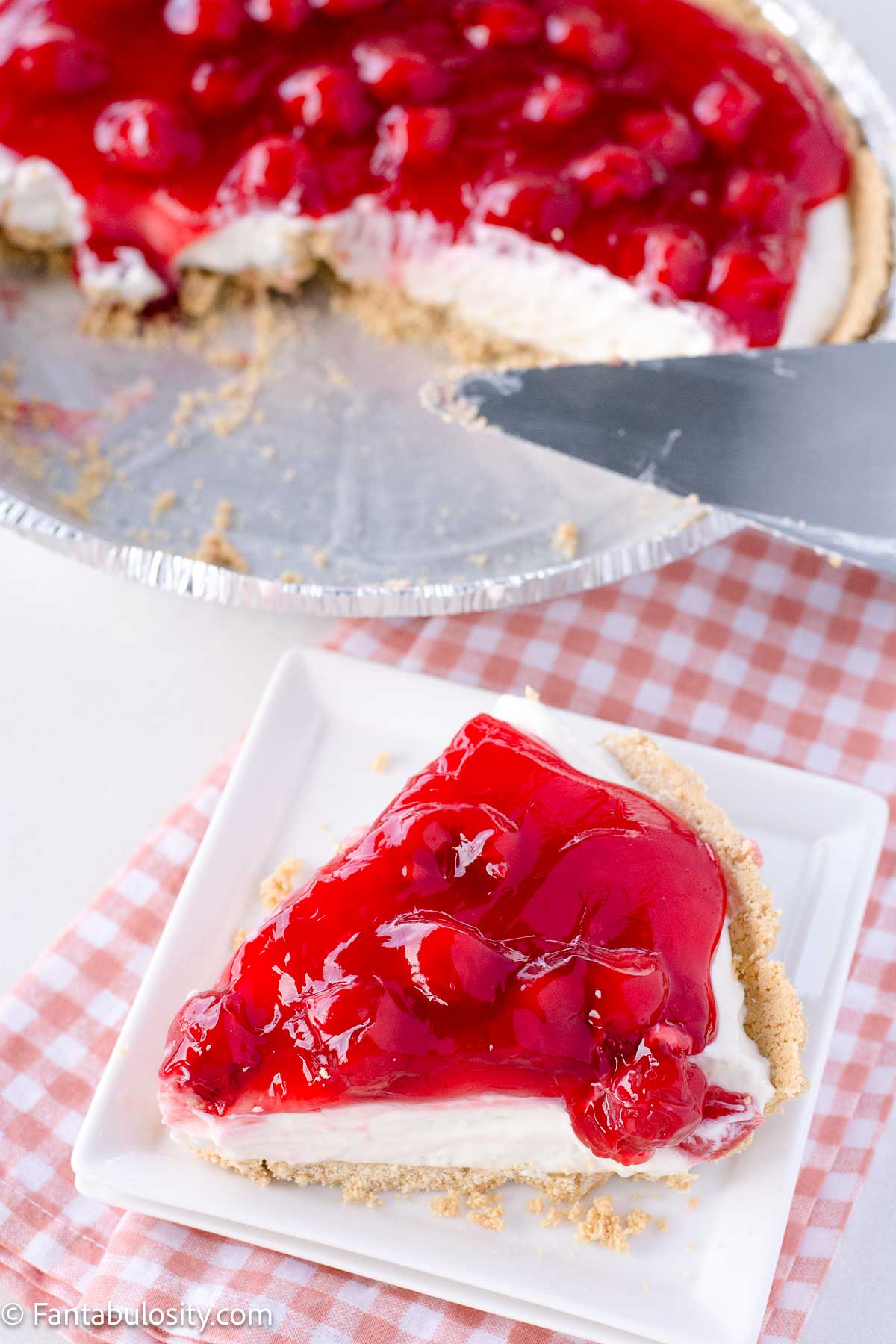 A slice of no bake cherry cheesecake on plate, next to pie plate.