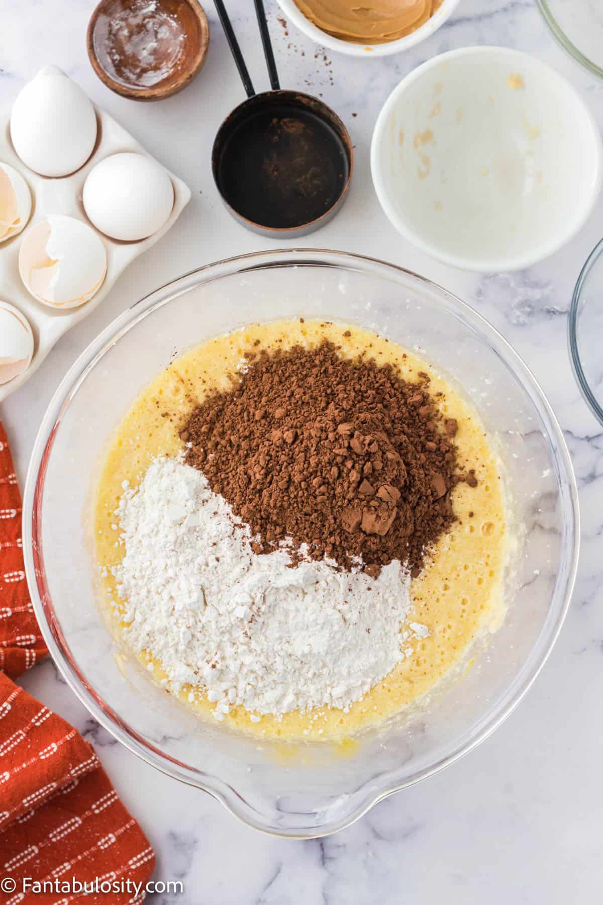 Flour and cocoa powder on top of the butter, sugar, egg, banana mixture in a bowl.