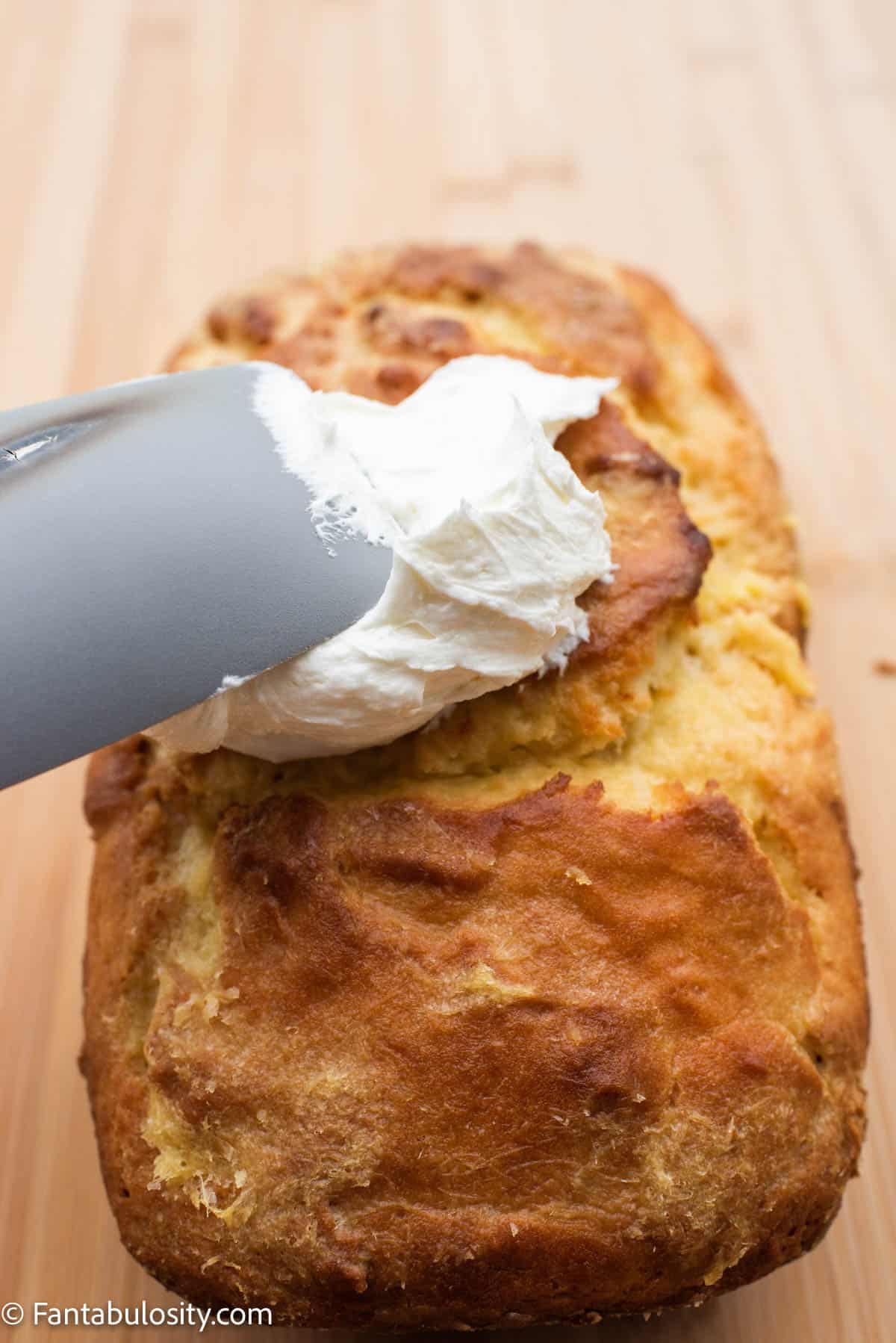 Icing being spread on a baked pineapple bread loaf.