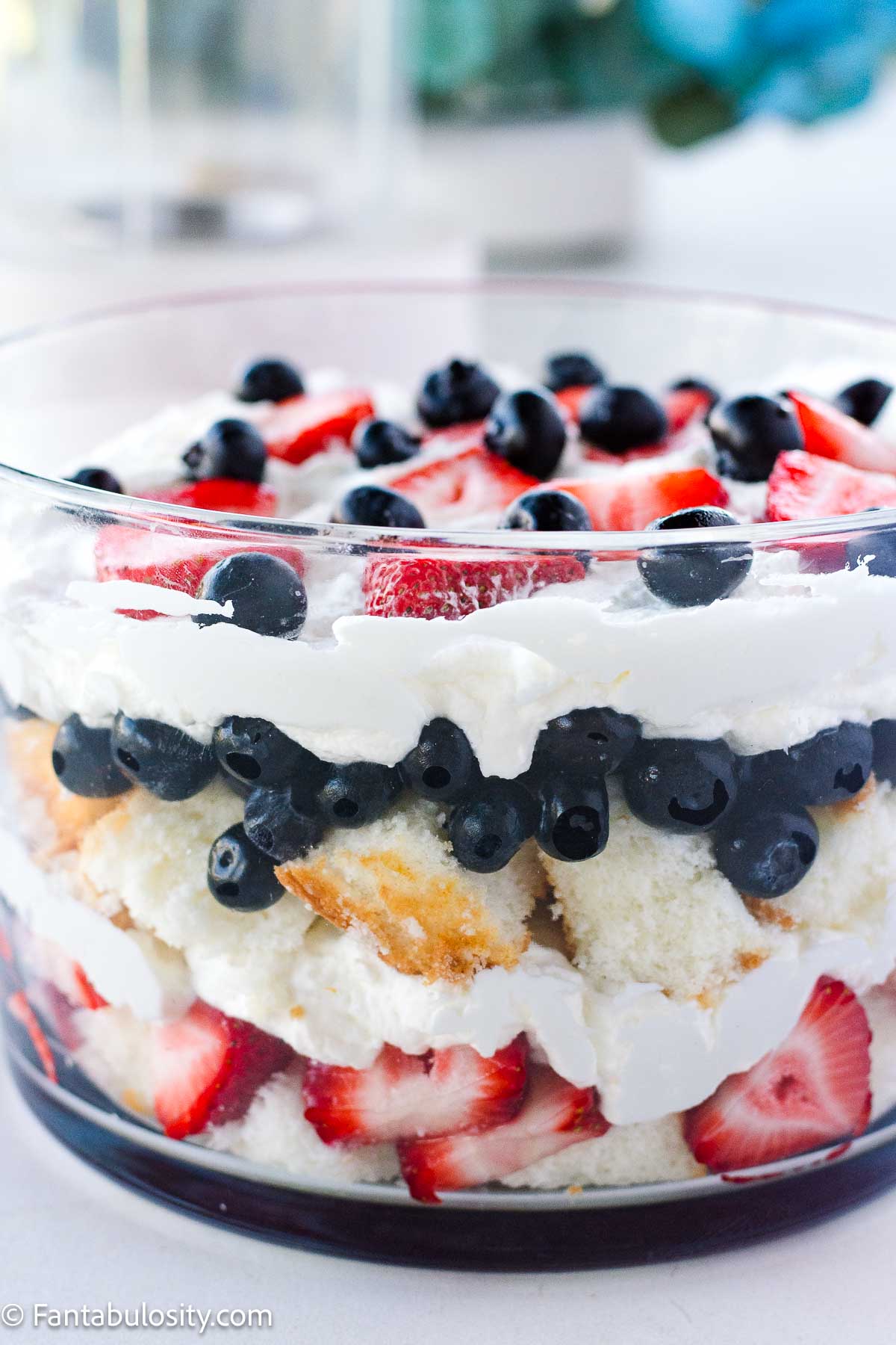 Strawberries, blueberries, angel food cake, and whipped cream, layered in a trifle bowl.