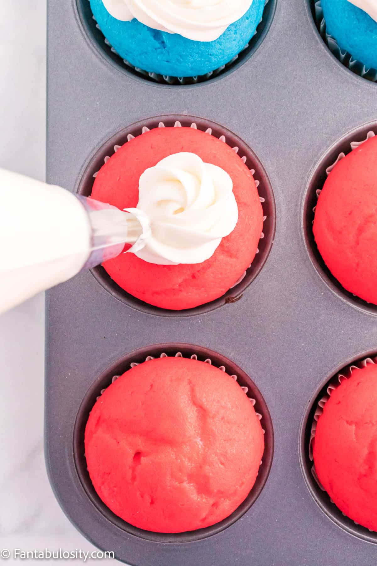 Frosting being piped on a red cupcake.
