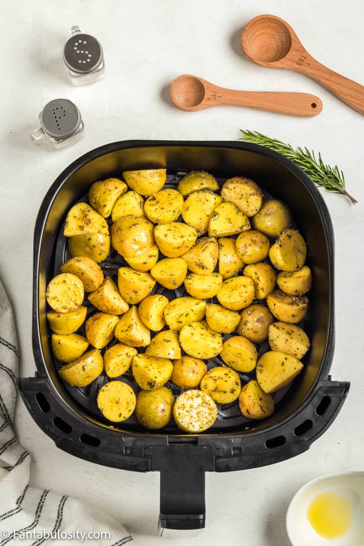 An air fryer basket with raw baby potatoes that are covered in oil and spices in it.