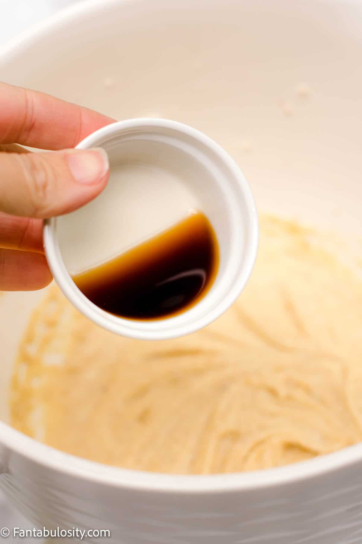 Creamed butter, sugar, and egg mixture in a bowl with someone pouring vanilla extract into the bowl.