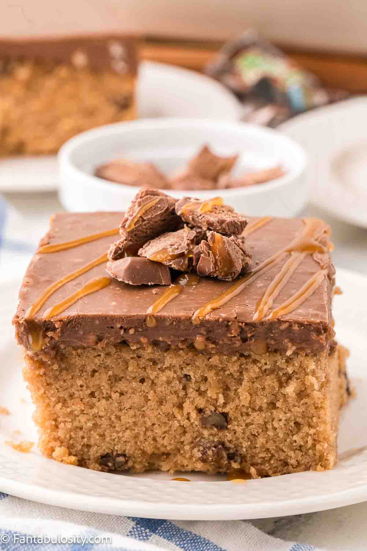 A piece of Milky Way sheet cake topped with candy bar pieces, sitting on a plate. 